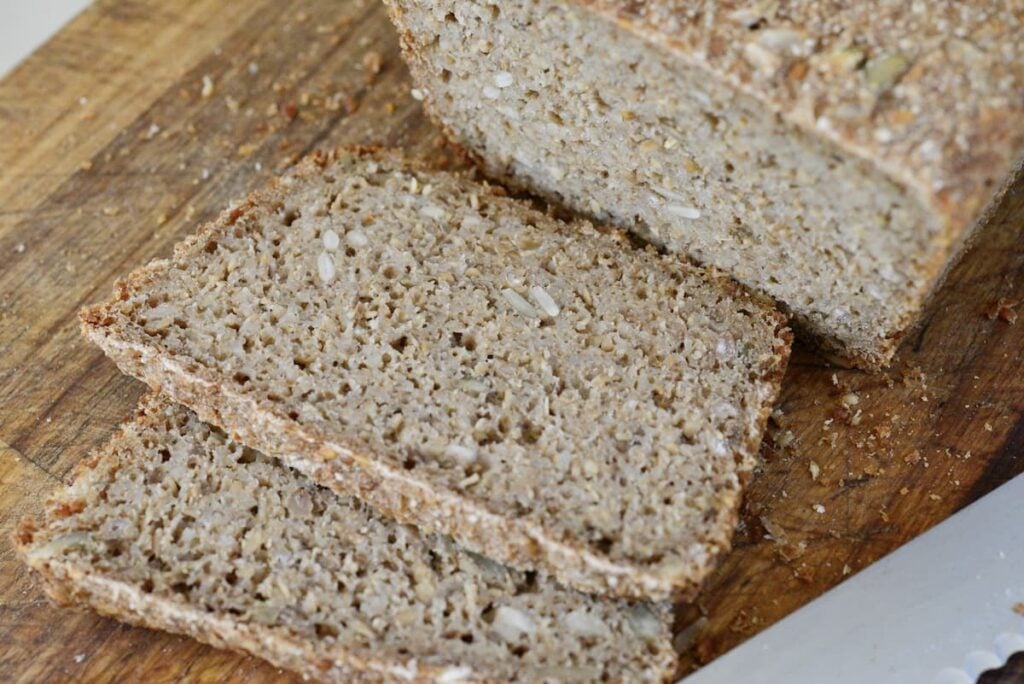 whole grain loaf of bread with two slices cut on cutting board