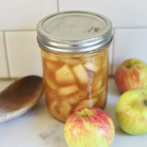 Mason jar with canned apple pie filling with apples and wooden spoon