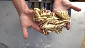 hands showing homemade fettucine over pasta machine