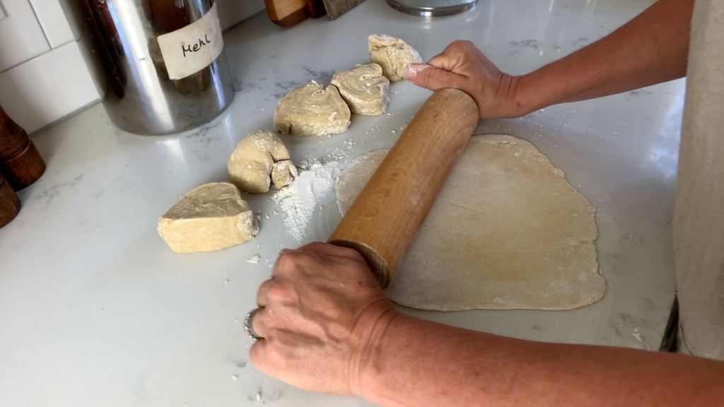 woman rolling out pasta dough on kitchen counter