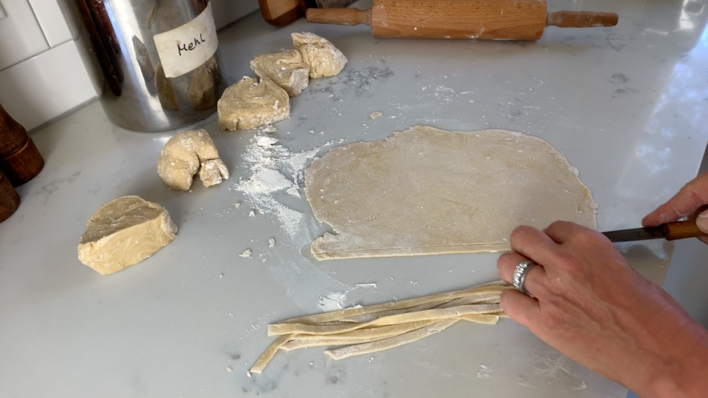 woman cutting pasta dough into long strips on kitchen counter