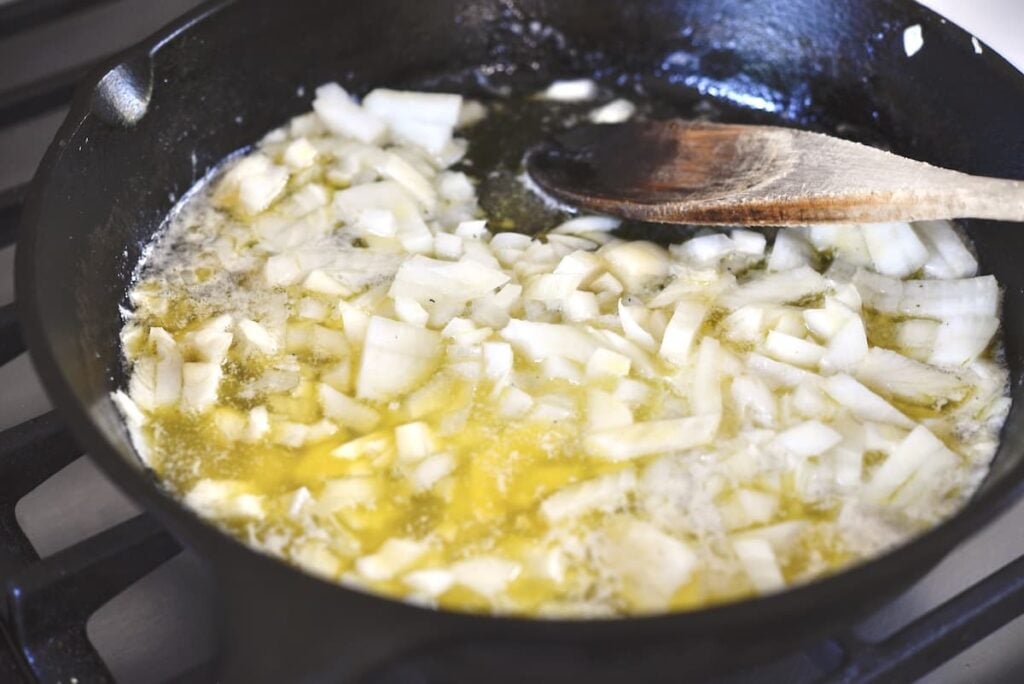 onions sauteeing in butter in cast iron skillet with wooden spoon