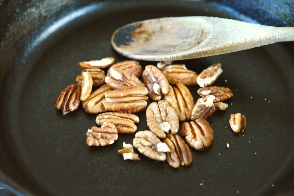 roasted nuts in cast iron skillet with wooden spoon