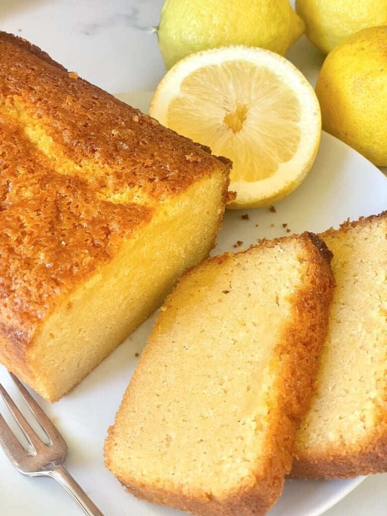 loaf of easy homemade sourdough lemon cake with slices on a plate with fork and lemon halves