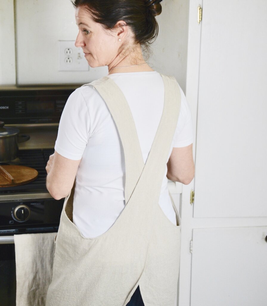 woman wearing cross-back apron in front of stove