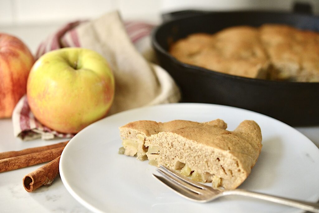 sourdough apple cake on plate with apples and cast iron skillet