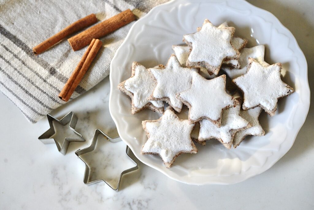cinnamon star cookies on plate with star-shaped cookie cutters and cinnamon sticks