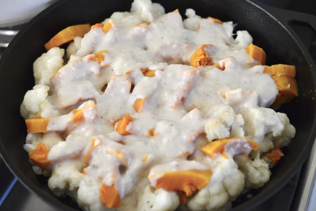 cauliflower and pumpkin in cast iron skillet with white sauce
