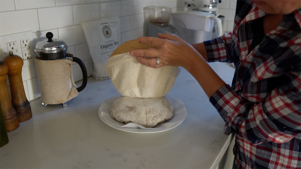 woman inverting rye sourdough from proofing basked onto parchment lined plate
