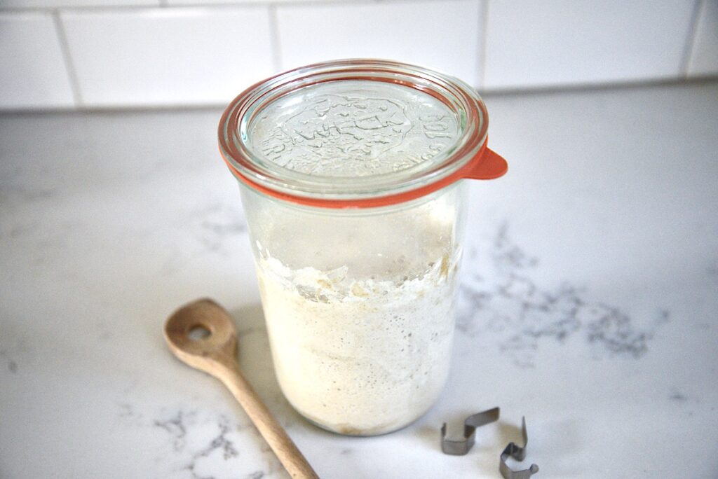 Weck jar with sourdough starter and wooden spoon on kitchen counter