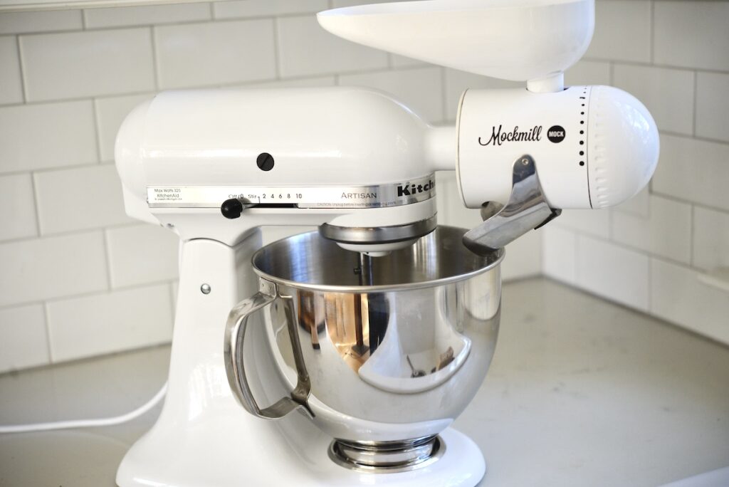 white Kitchenaid stand mixer with grain mill attachment on kitchen counter
