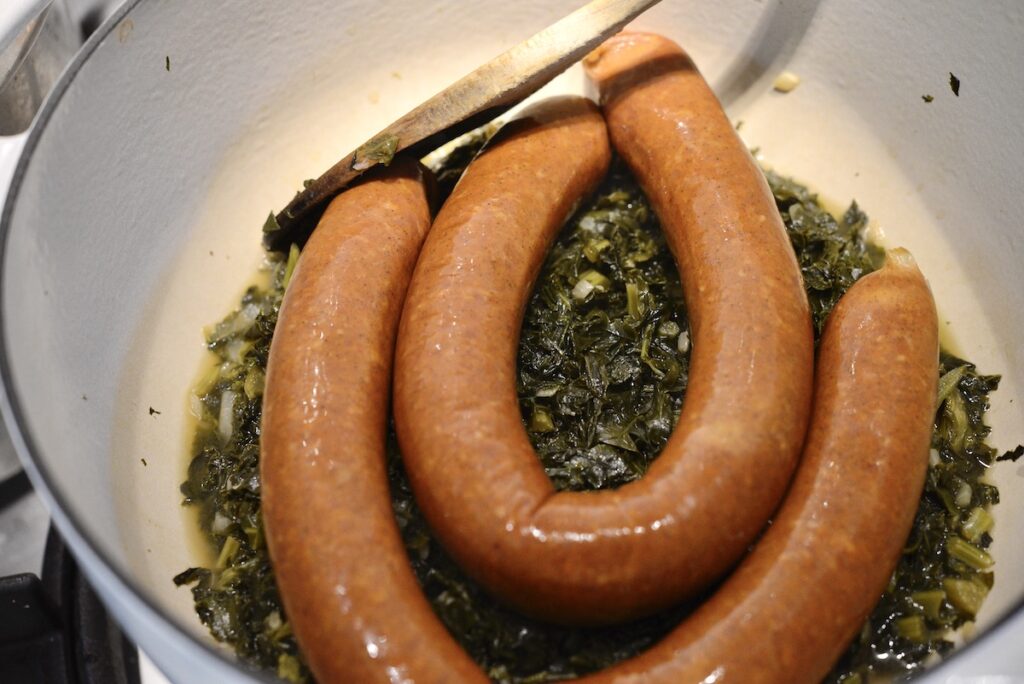 sausages and braised kale in pot with spoon