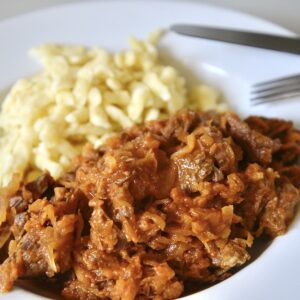 Hungarian beef goulash with egg noodles on a plate with utensils