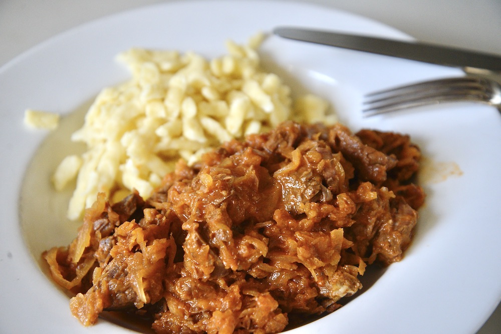 Hungarian beef goulash and German spaetzle on plate with fork and knife