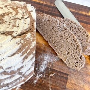 loaf of rye bread with 2 slices cut on wooden board