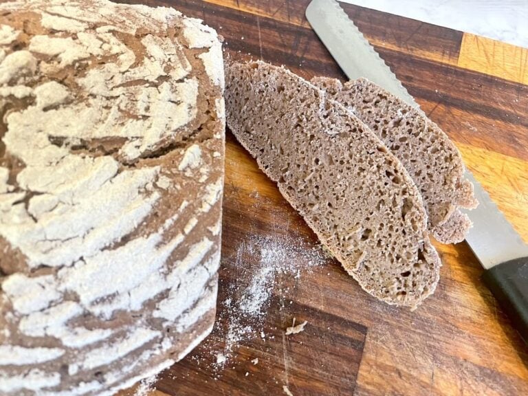 loaf of rye bread with 2 slices cut on wooden board