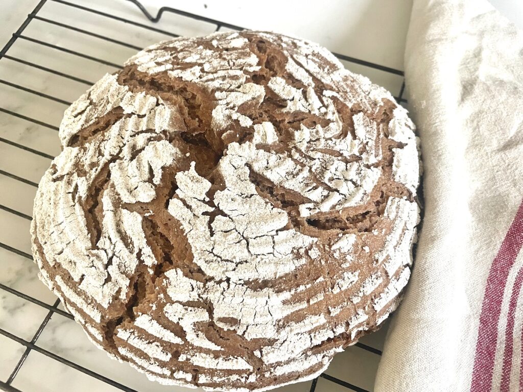 loaf of sourdough rye bread on wire rack with kitchen towel