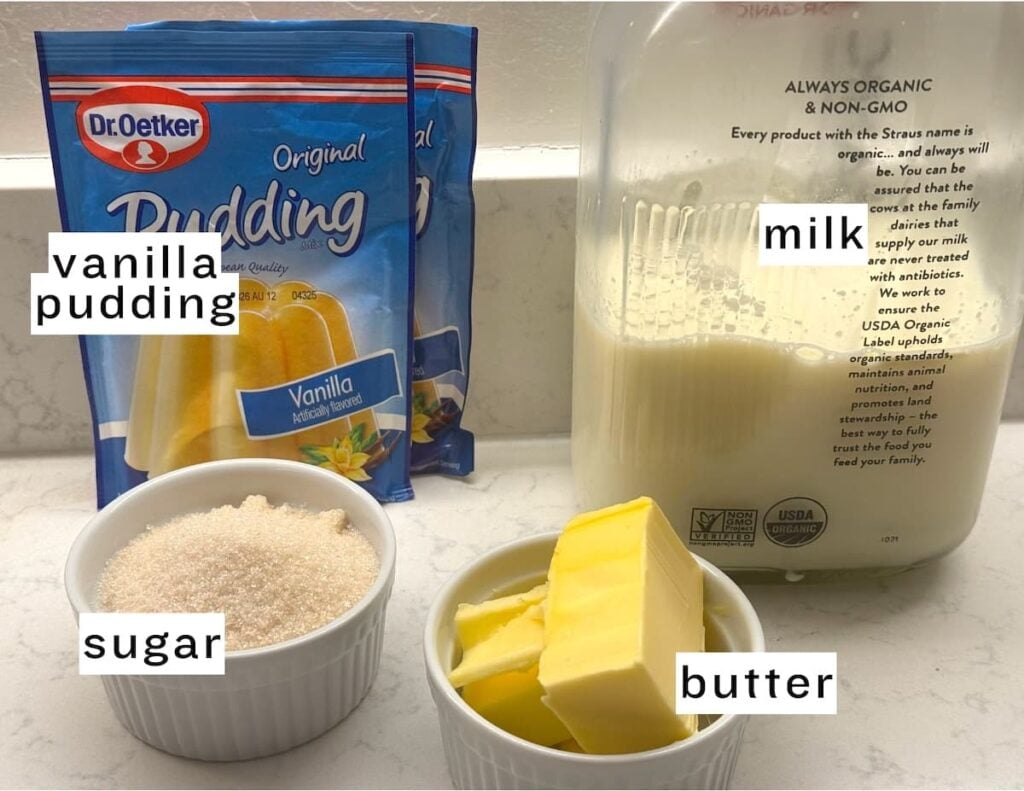 Packets of vanilla pudding mix, a glass bottle of milk, a ramekin of sugar, and a ramekin with sliced butter are displayed on a kitchen counter. Each item is labeled with its name.