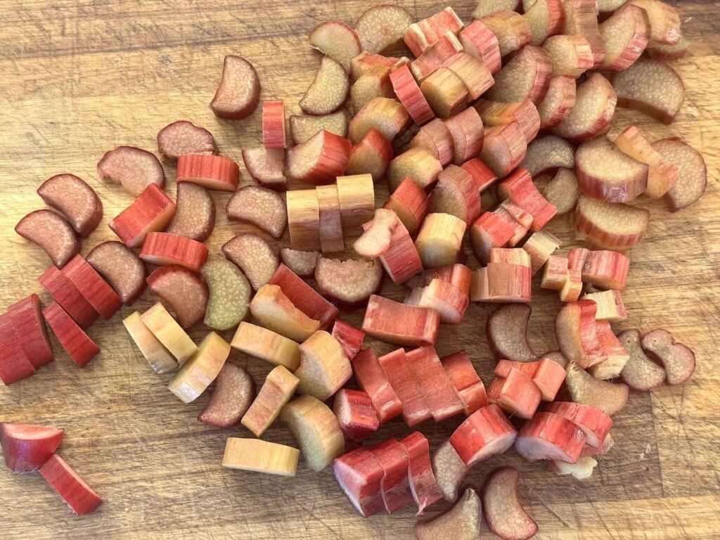 Chopped rhubarb pieces with red and light green hues scattered on a wooden cutting board.