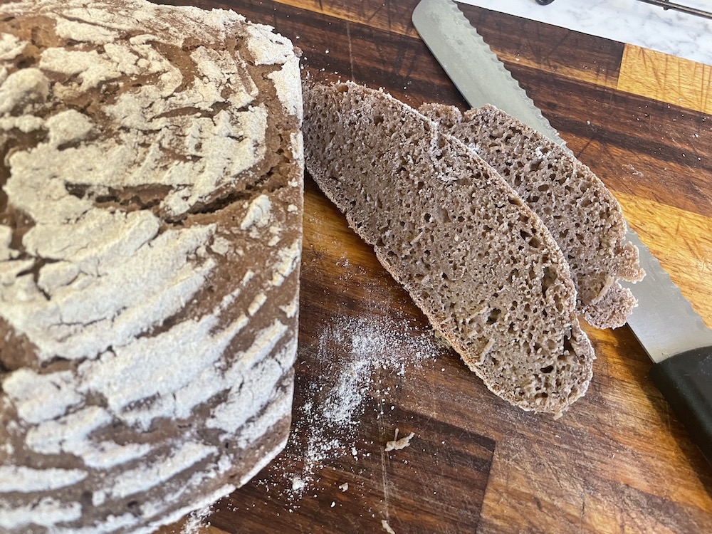 loaf of sourdough rye bread and slices with bread knife on cutting board