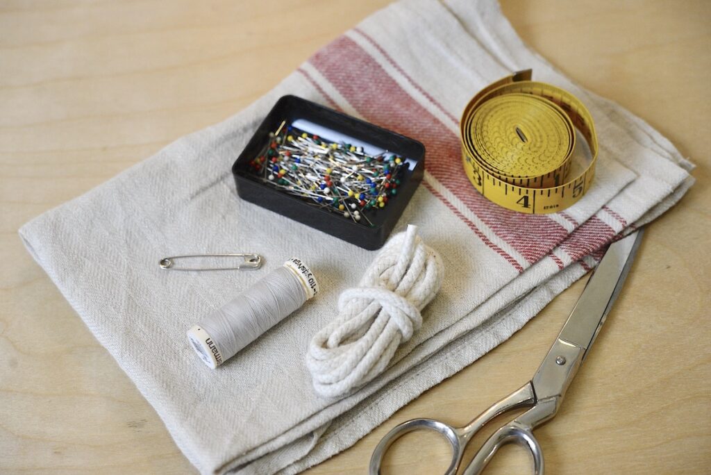 linen tea towel, scissors, cord, thread, safety pin, pins, and measuring tape