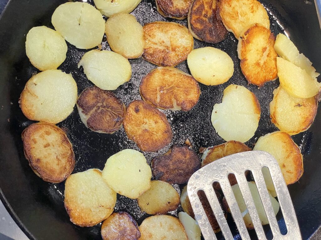 fried potato slices in cast iron skillet with stainless steel spatula