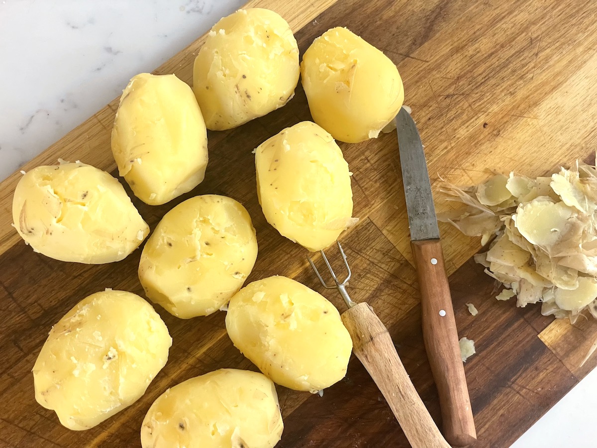 Peeled yellow potatoes on a wooden cutting board.