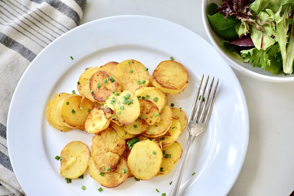 German fried potatoes on plate with fork and green salad on the side