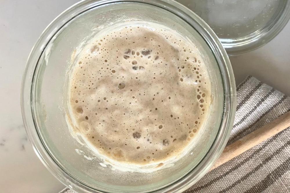 sourdough starter in glass jar with kitchen towel