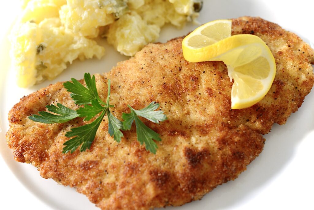 German schnitzel with lemon, parsley, and potato salad in background