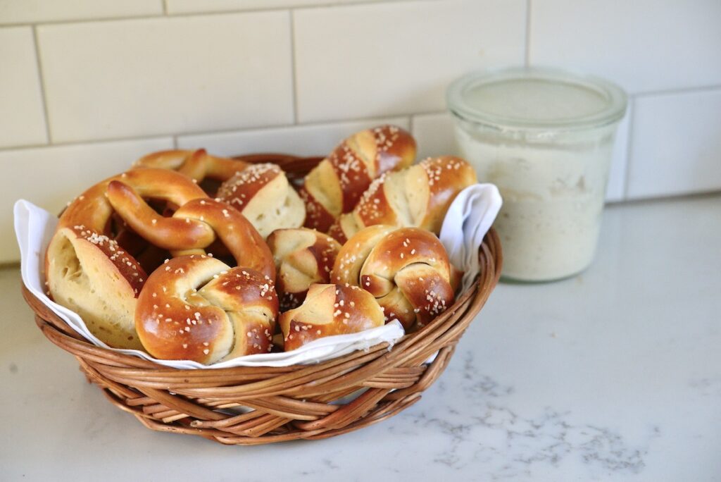 sourdough pretzel shapes in basket with sourdough starter in background 