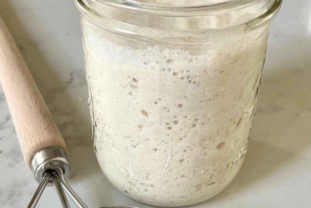 sourdough starter in glass jar with Danish whisk