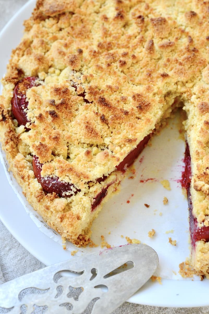 plum streuselkuchen with one slice missing, on a cake plate.