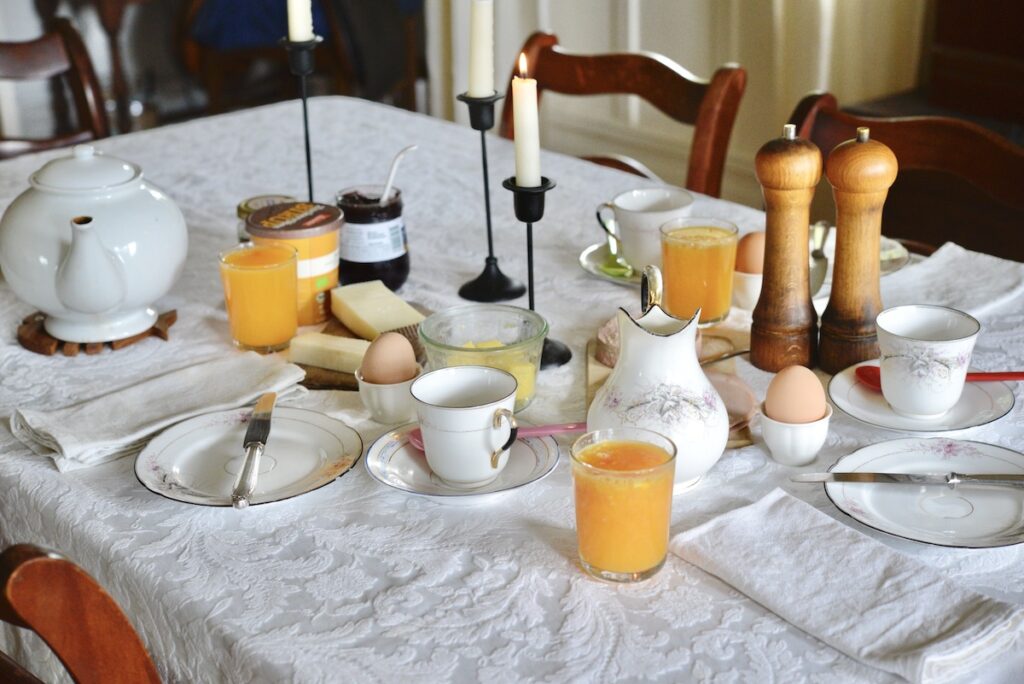 breakfast table set with china, orange juice, eggs, candles on white table cloth