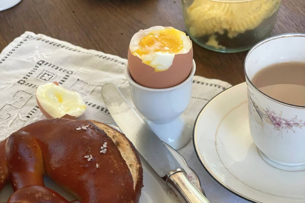 soft boiled egg cut open next to plate with pretzel and coffee cup