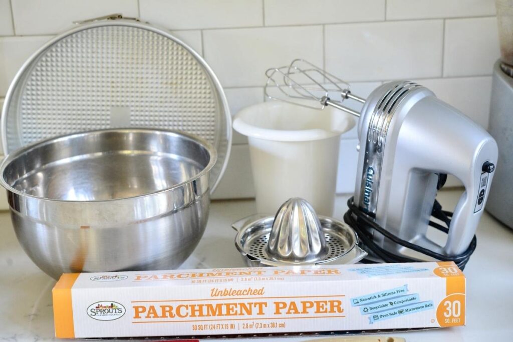 tools for making German cheesecake: mixing bowl, springform pan, electric handmixer, tall bowl, citrus press, parchment paper