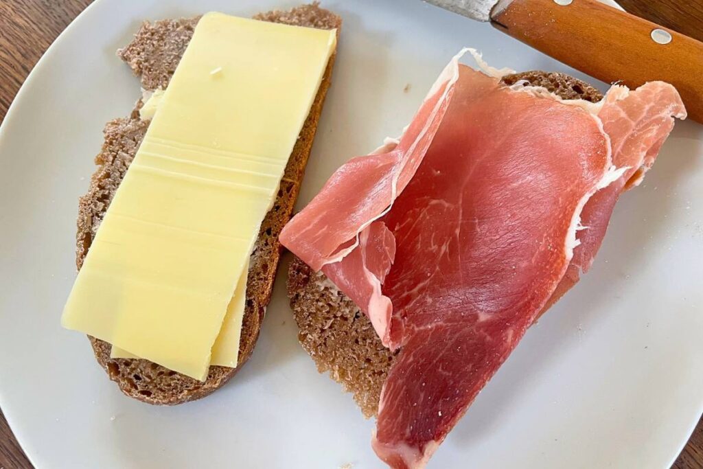 2 slices of rye bread with cheese and prosciutto on plate