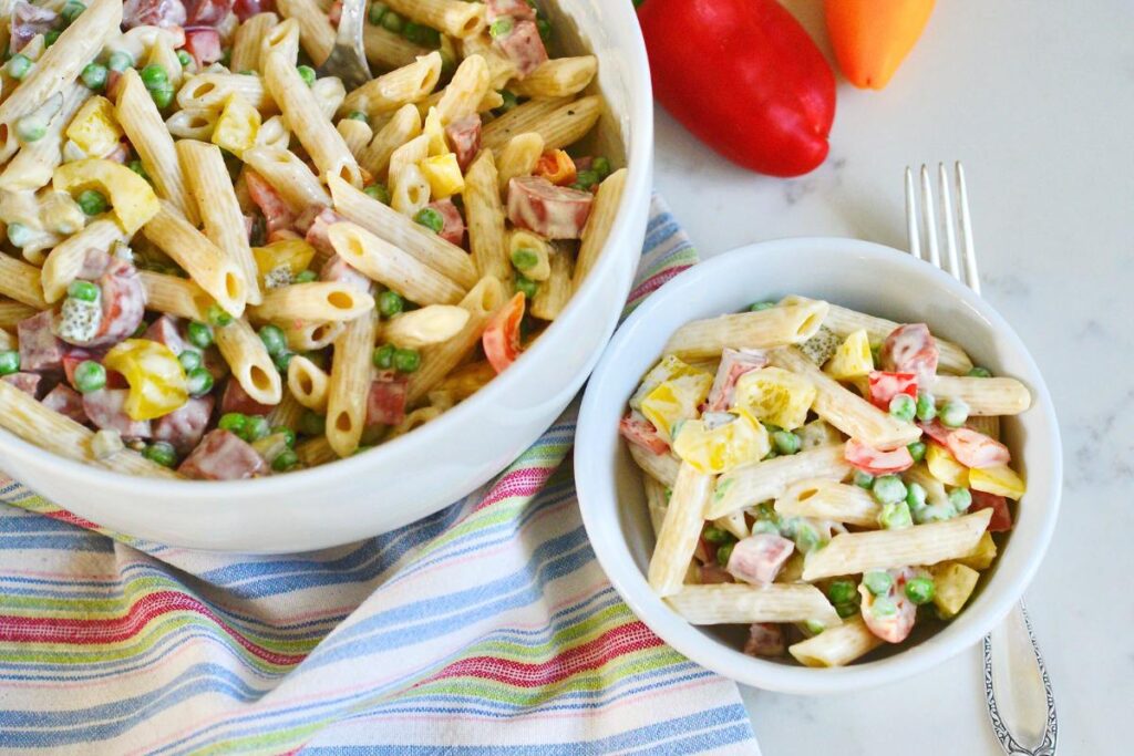 2 white bowls with cream German pasta salad with fork on kitchen counter