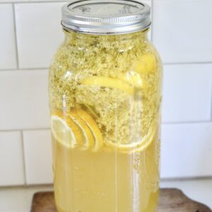 large jar of elderflower syrup with lemon slices in it