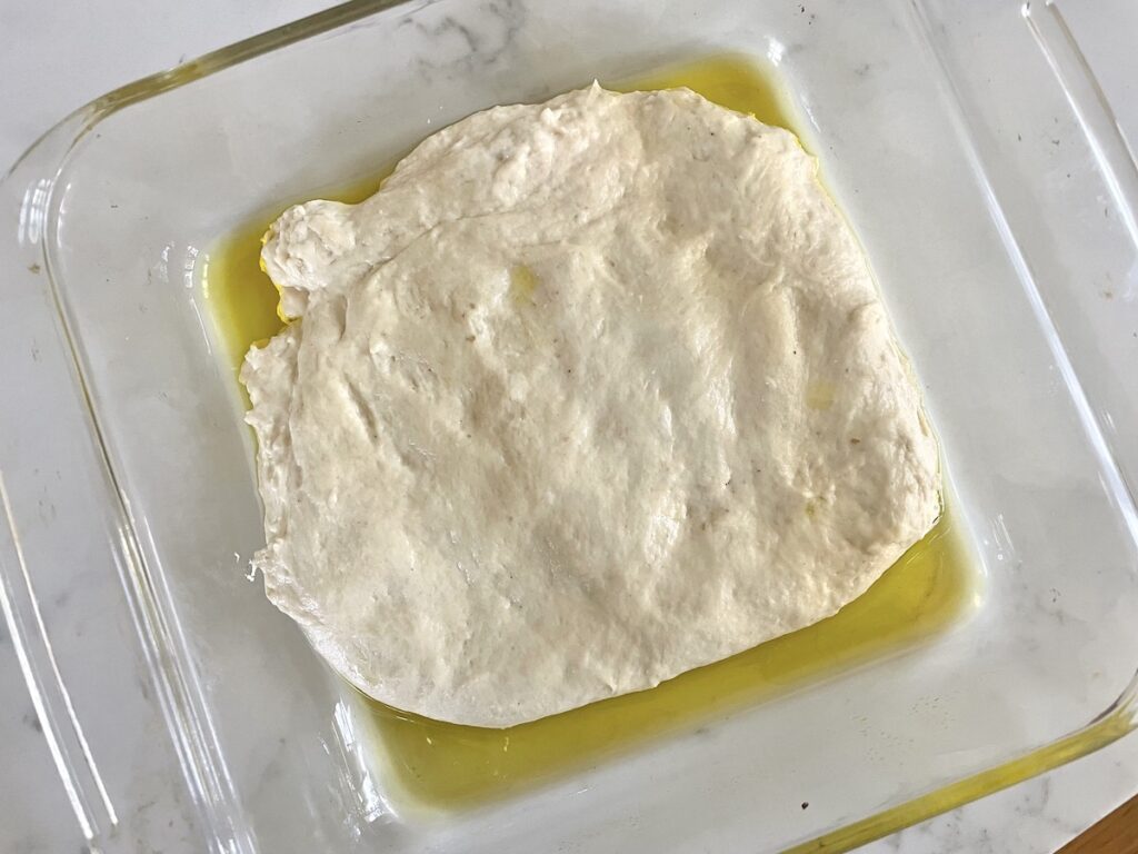 sourdough focaccia dough in square glass baking dish with olive oil