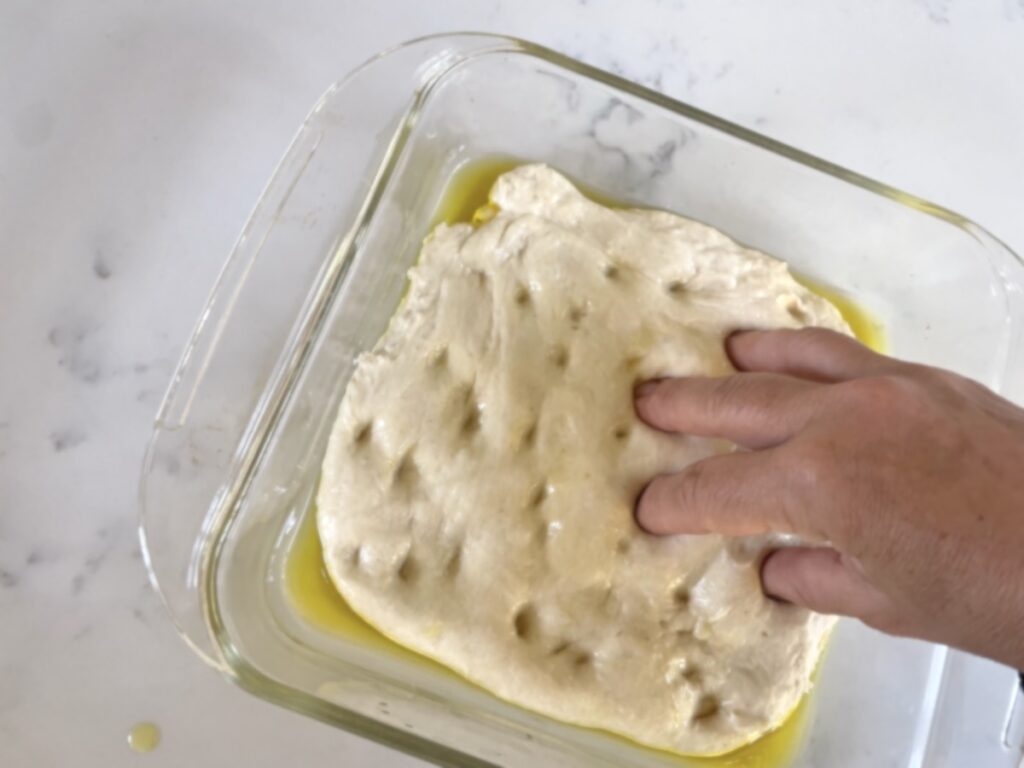 fingers pressing dimples into surface of sourdough focaccia
