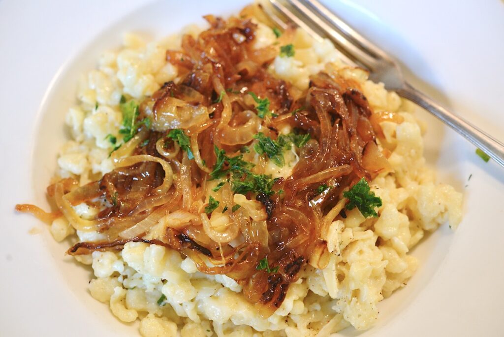 German spaetzle with fried onions, chopped parsley and fork on white plate