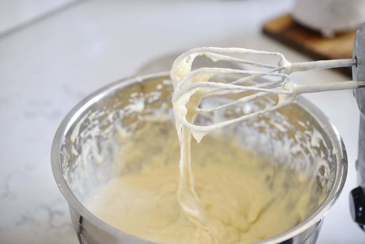 German spaetzle batter dripping off of electric mixer beaters into a large metal mixing bowl.