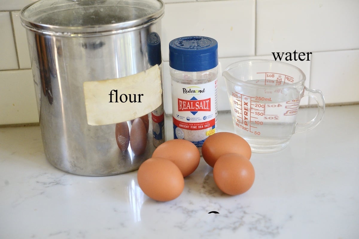jar of flour, shaker of salt, measuring cup with water, and 4 eggs on a kitchen counter.