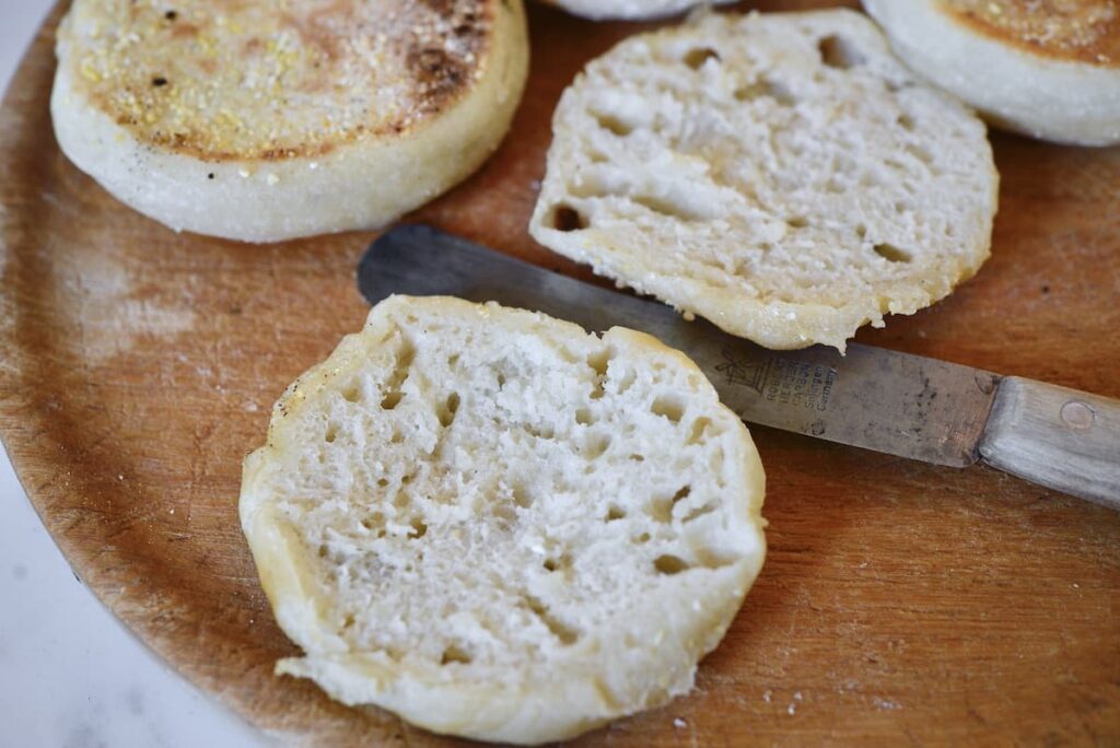 sourdough English muffin cut open on wooden cutting board with knife