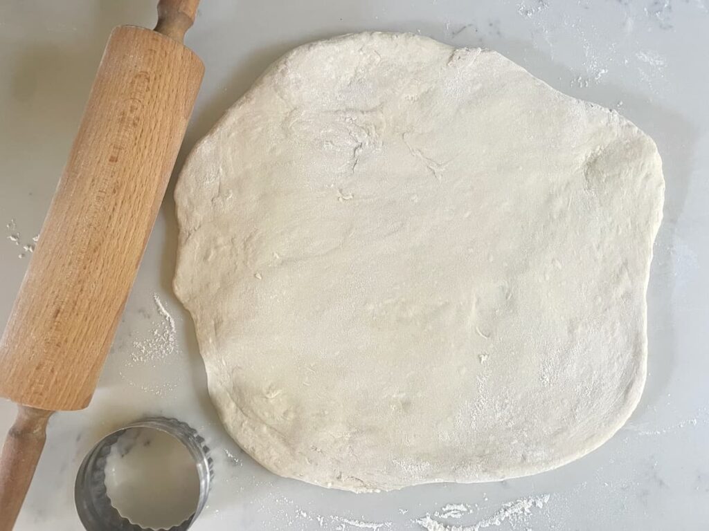 sourdough English muffin dough rolled out with rolling pin and biscuit cutter