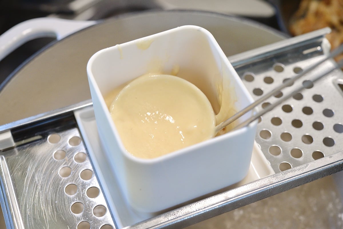 Ladle with batter sitting in a spaetzle maker.