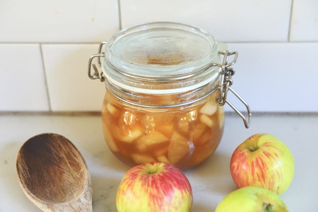 canning jar with apple pie filling on kitchen counter with apples and wooden spoon