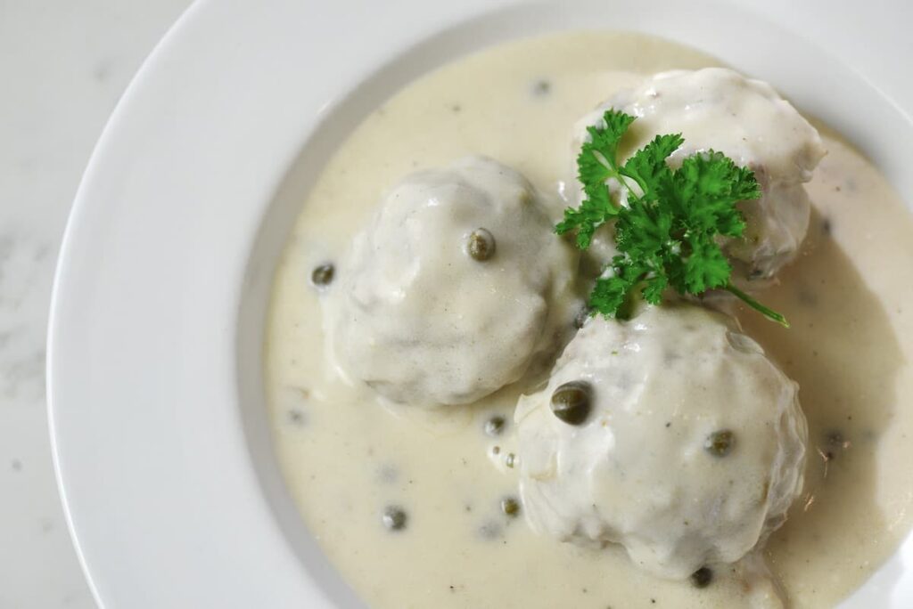 3 Königsberger Klopse on white plate with white sauce and fresh parsley