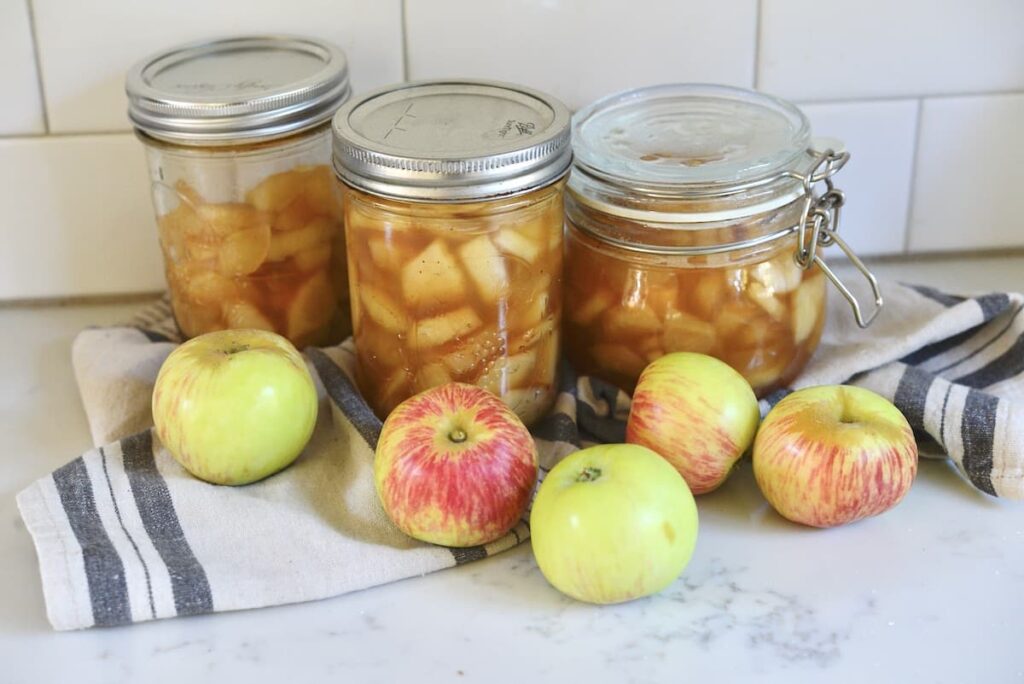 canning jars with apple pie filling on kitchen counter with apples and tea towel